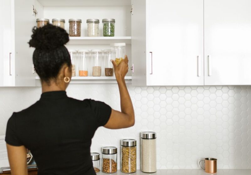 A woman organizing a pantry shelf with various food jars in a modern kitchen.