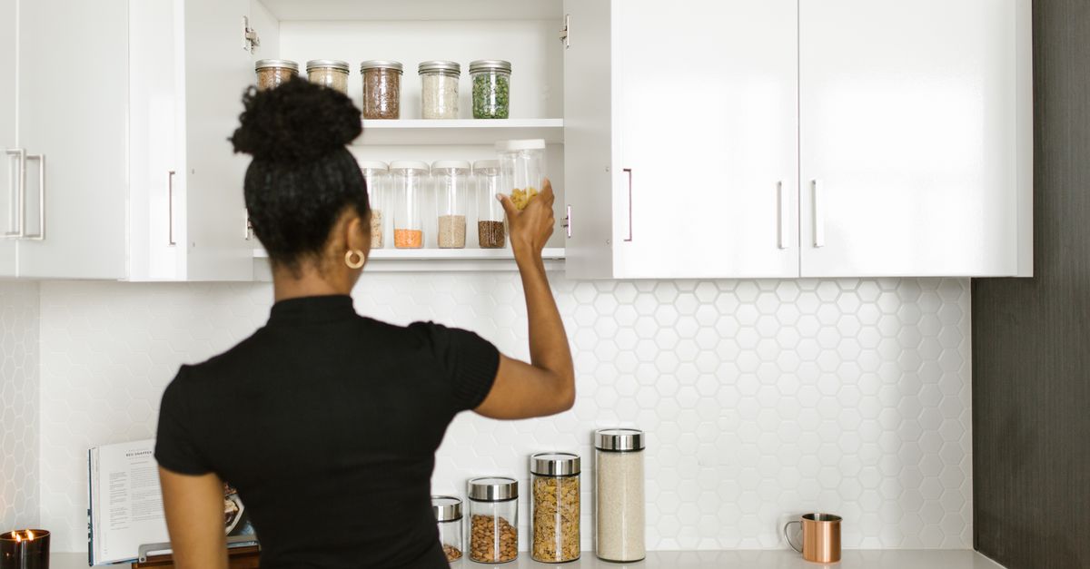 A woman organizing a pantry shelf with various food jars in a modern kitchen.