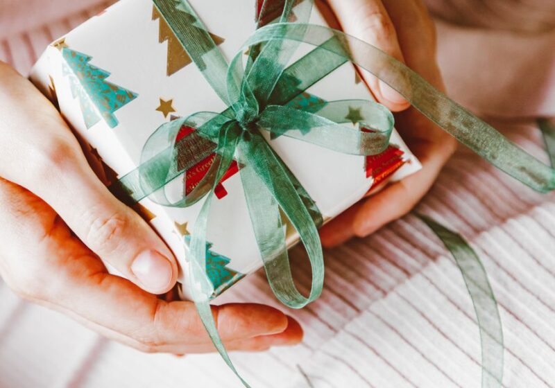 Symbolic Christmas gift wrapped in holiday-themed paper with green ribbon, held in hands.