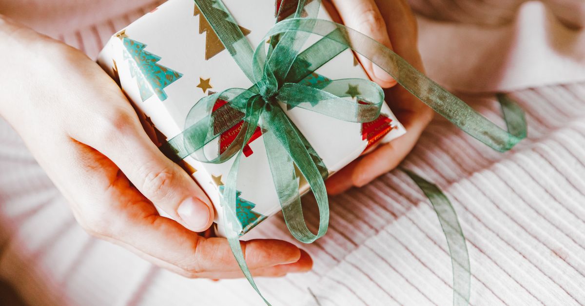 Symbolic Christmas gift wrapped in holiday-themed paper with green ribbon, held in hands.