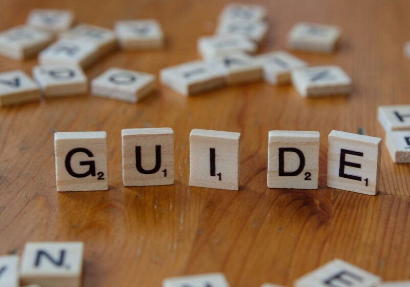 A wooden table topped with scrabble tiles spelling the word guide