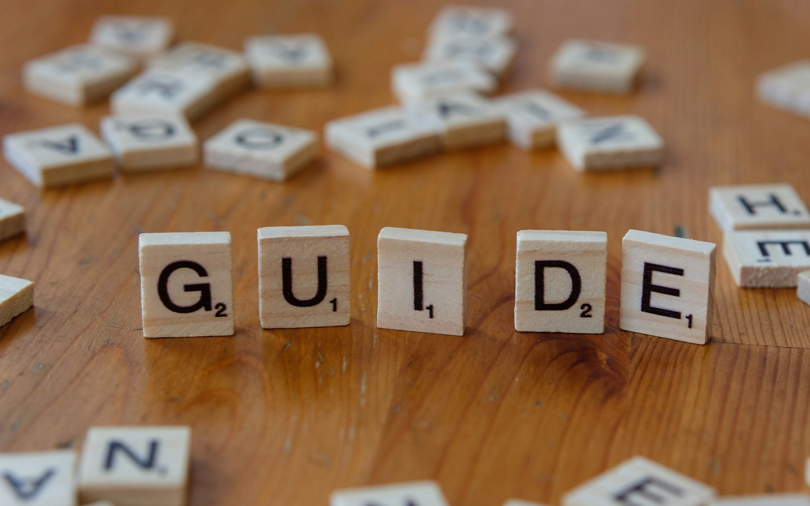 A wooden table topped with scrabble tiles spelling the word guide
