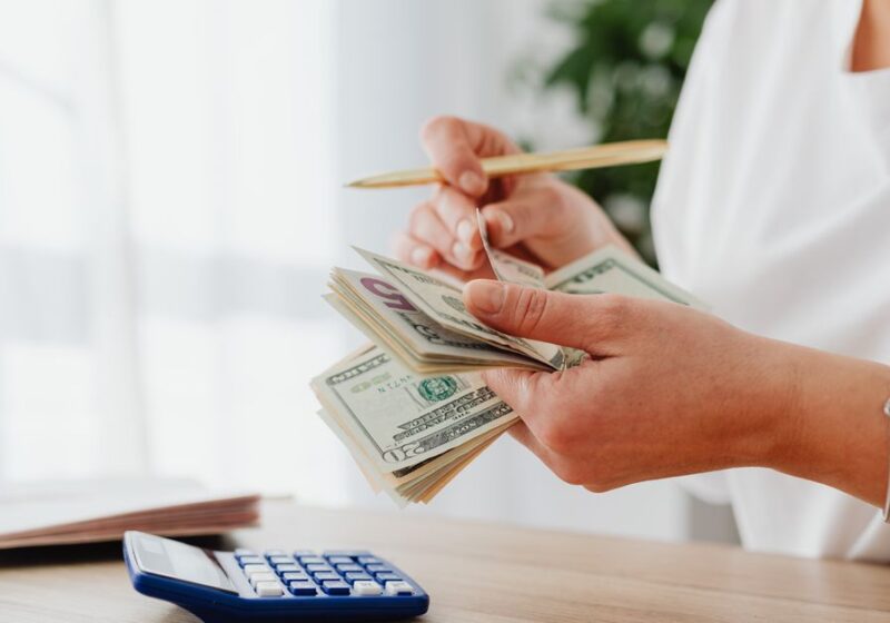 Close-up of a woman holding US dollars, calculating finances at home.