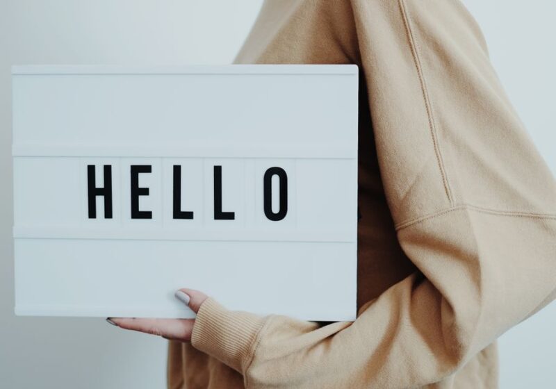 A person holding a lightbox displaying the word 'HELLO' on a white background.