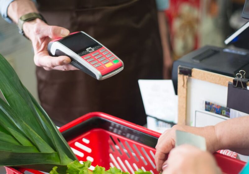 A customer using a contactless payment method at a grocery store checkout with fresh produce.