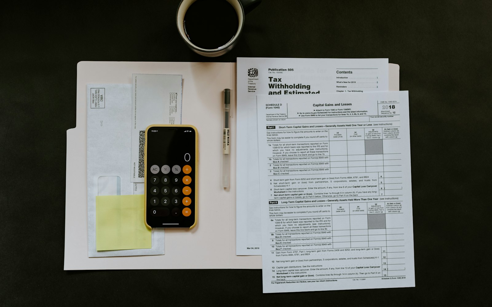 black Android smartphone near ballpoint pen, tax withholding certificate on top of white folder