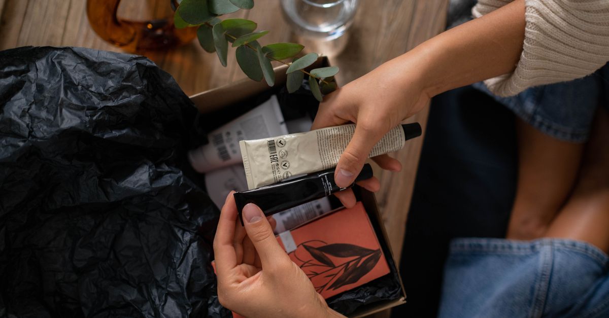 Hands unboxing skincare products with eucalyptus on wooden surface.