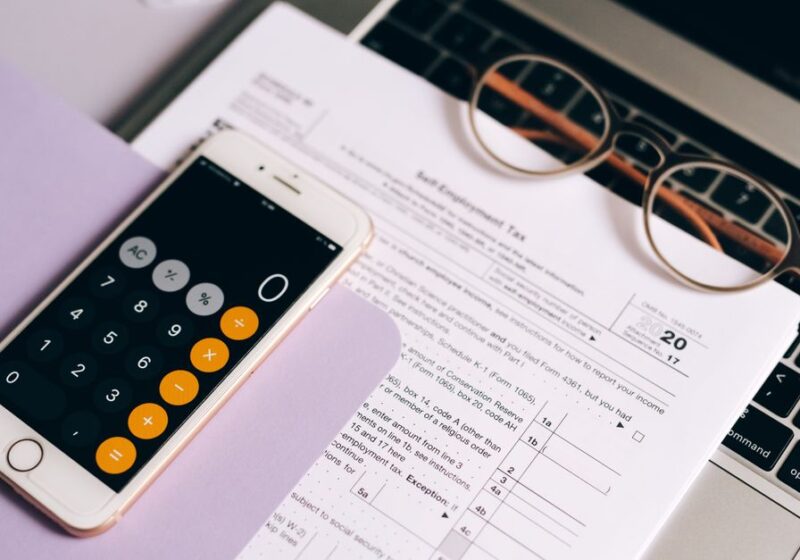 A smartphone with a calculator app on tax documents next to a laptop, emphasizing modern accounting.