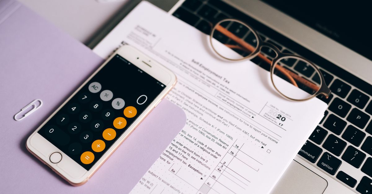 A smartphone with a calculator app on tax documents next to a laptop, emphasizing modern accounting.