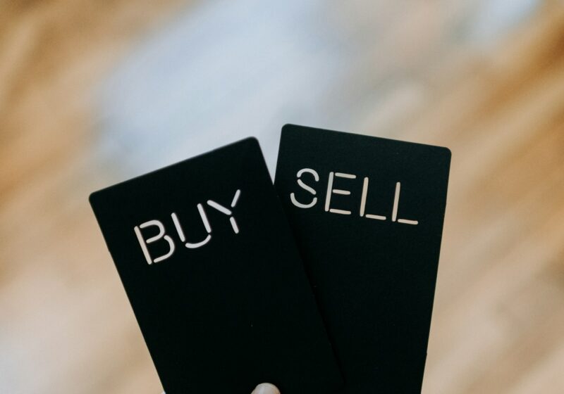 a hand holding two black cards with the words buy and sell written on them