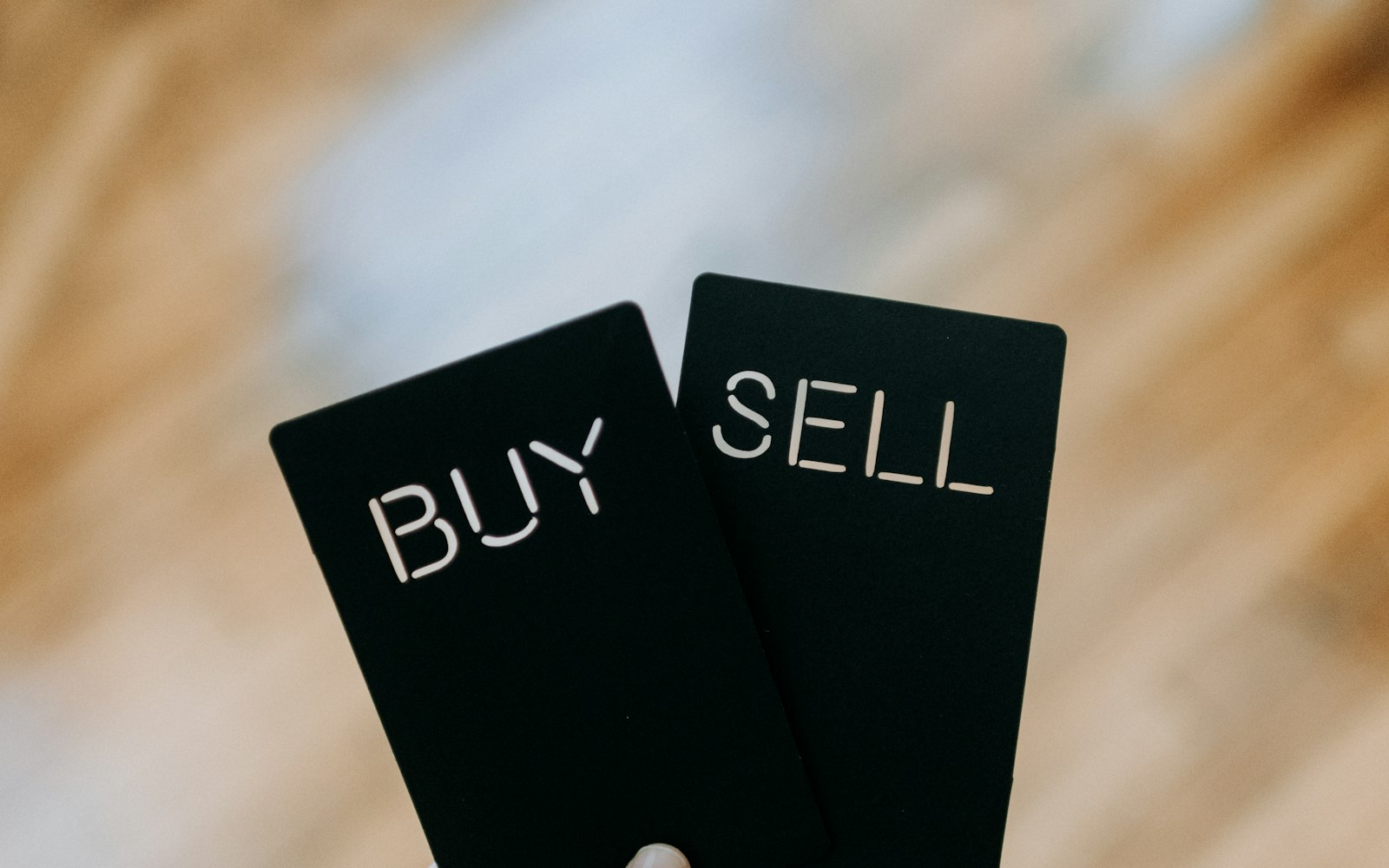 a hand holding two black cards with the words buy and sell written on them