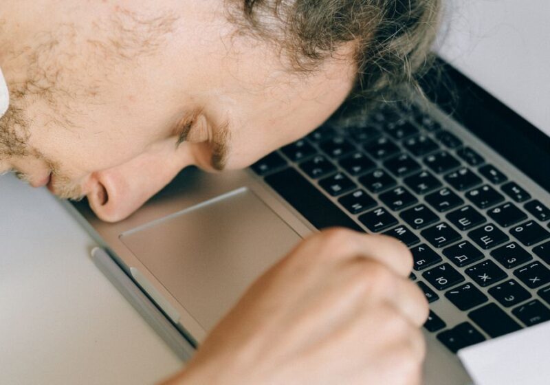 Exhausted employee resting head on laptop keyboard due to burnout and stress.