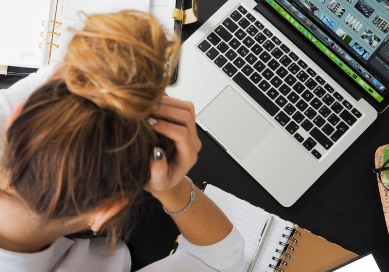 Overhead view of a stressed woman working at a desk with a laptop, phone, and notebooks.
