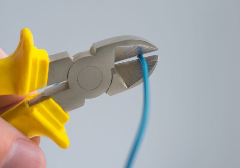 Detailed image of a hand using yellow-handled pliers to cut a blue wire.
