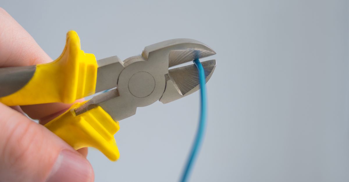 Detailed image of a hand using yellow-handled pliers to cut a blue wire.