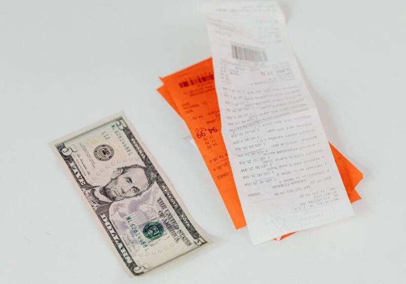 Close-up of a five-dollar bill next to shopping receipts on a white background, ideal for finance and retail themes.