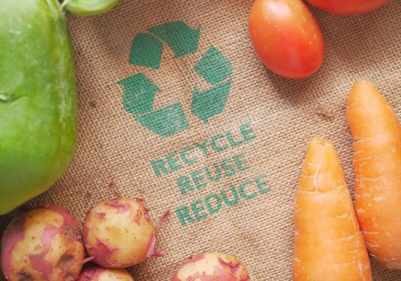 Fresh vegetables on a burlap bag with recycle symbol, promoting eco-friendly choices.