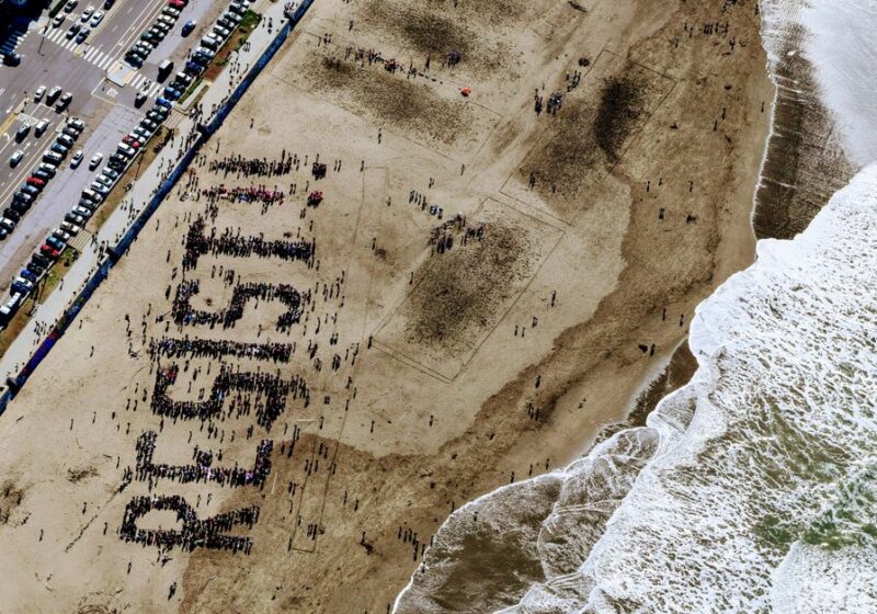 A large group on a beach forms the word "Resist" in powerful demonstration.