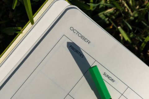 A planner and pen on grass with October page open, illuminated by sunlight.