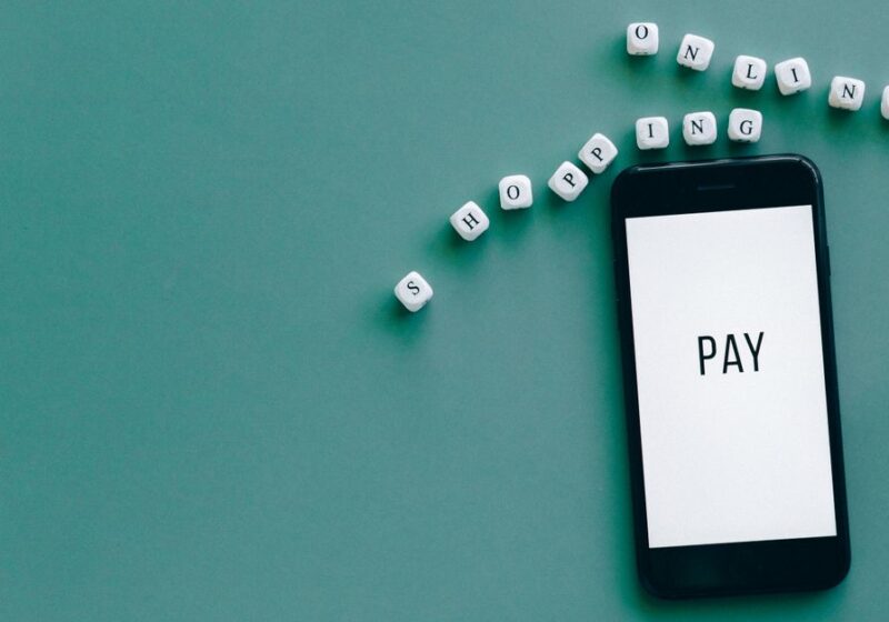 Image of smartphone displaying 'PAY' surrounded by dice spelling 'online shopping' on teal background.
