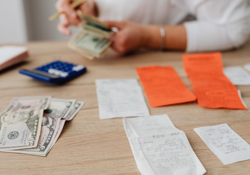 A person using a calculator and cash to plan a household budget.
