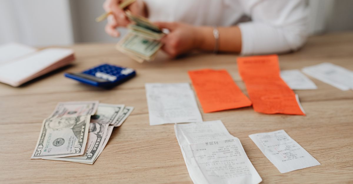 A person using a calculator and cash to plan a household budget.