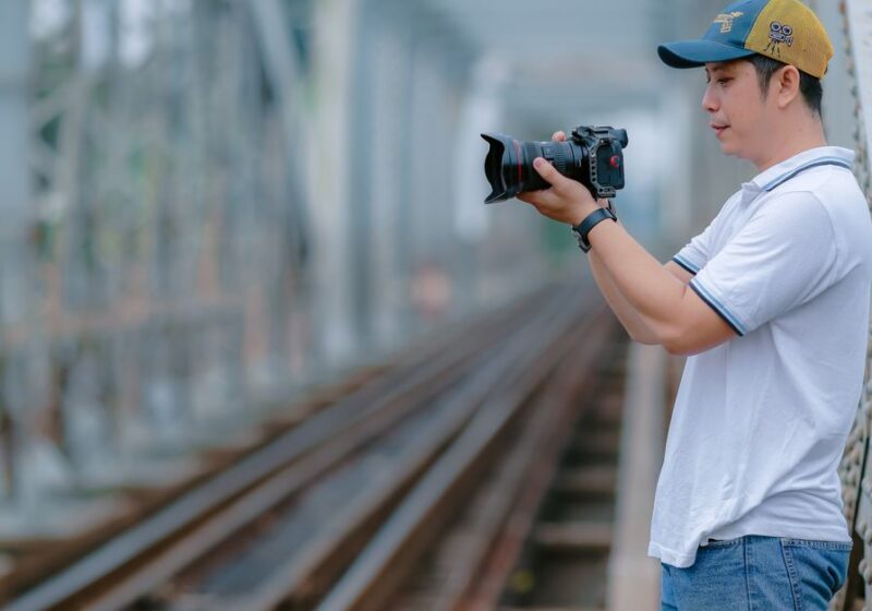 A photographer on a railway bridge capturing scenic moments with his camera.