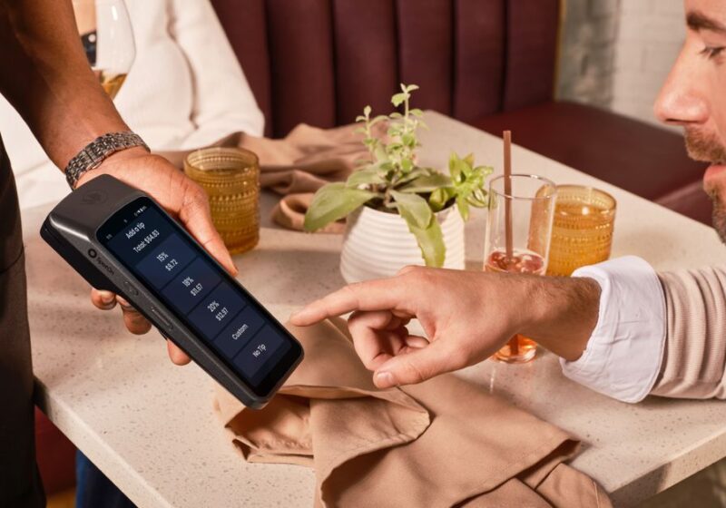 A diner uses a handheld POS system for digital tipping in a casual restaurant setting.