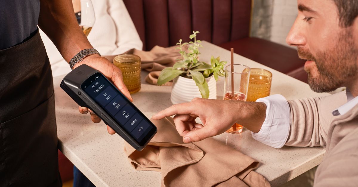 A diner uses a handheld POS system for digital tipping in a casual restaurant setting.