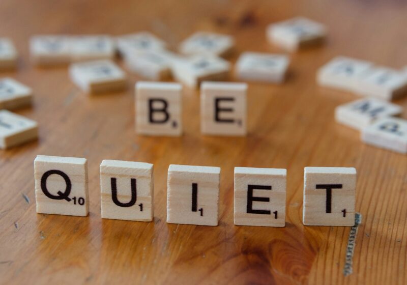 The word be quiet spelled with scrabble letters on a wooden table