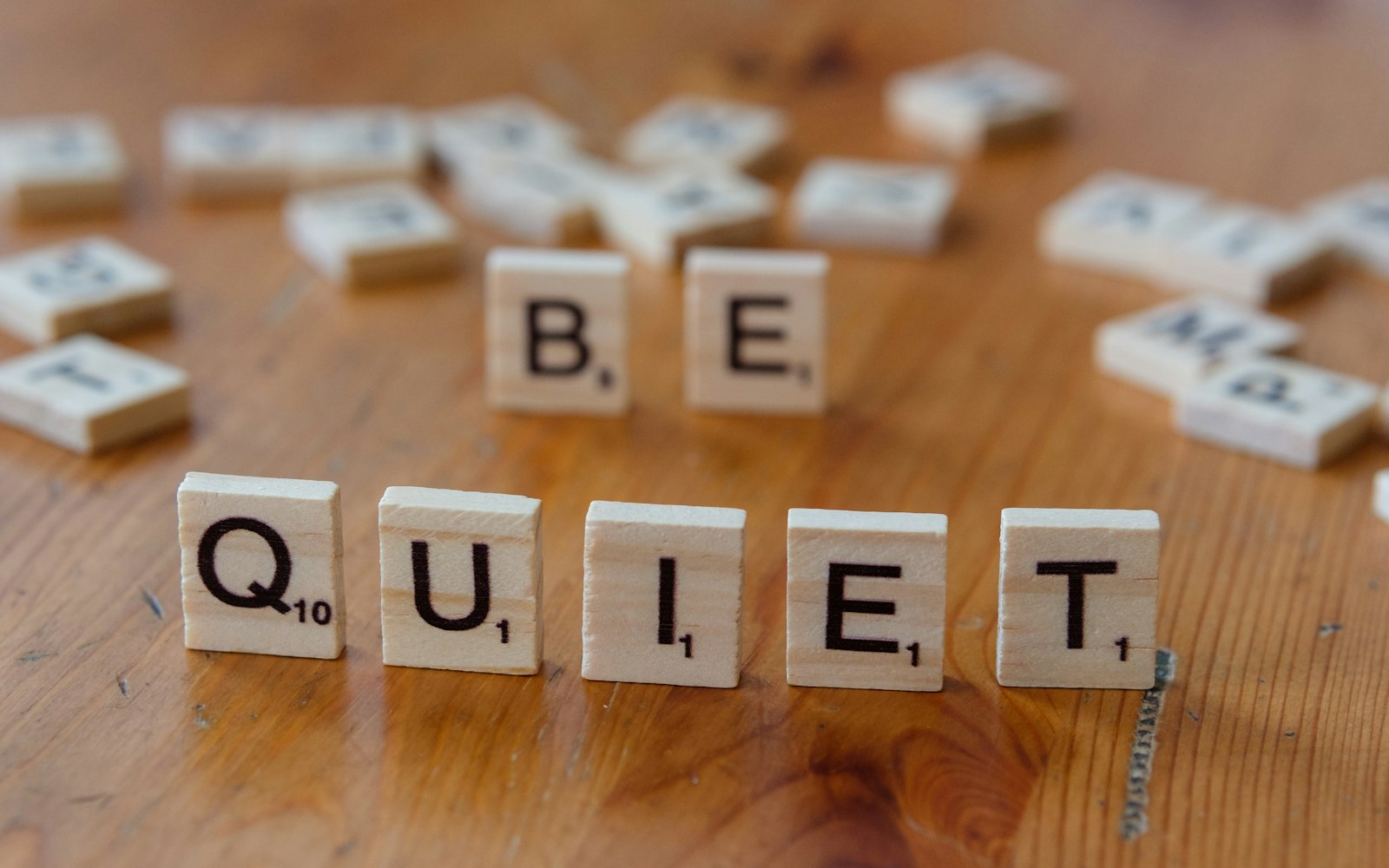 The word be quiet spelled with scrabble letters on a wooden table