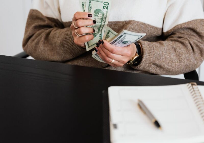 Close-up of an adult counting dollar bills at a desk with a notebook.