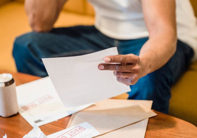 Man sitting on sofa reading unpaid bills, looking stressed and concerned over financial debt.