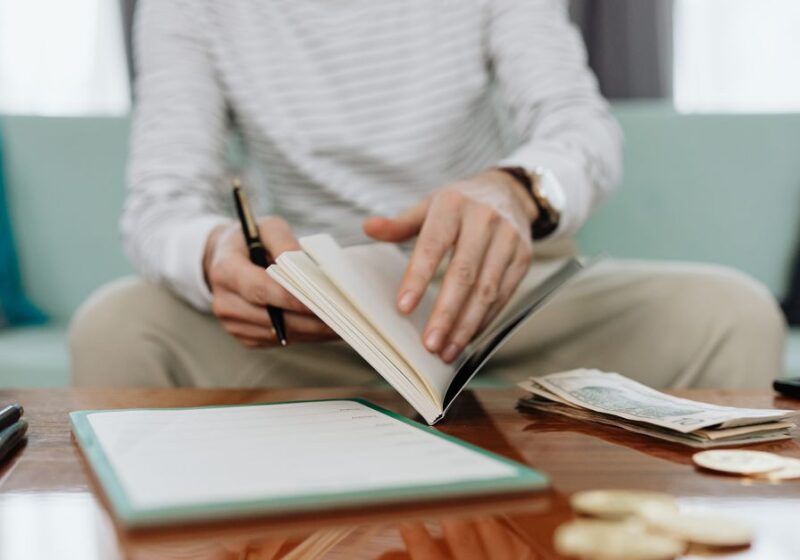 Individual reviewing finances at a table with notebook, money, and laptop.