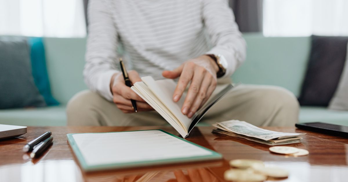 Individual reviewing finances at a table with notebook, money, and laptop.